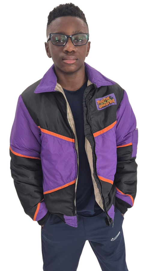 A young boy wearing a stylish jacket. Purple, orange and black. The jacket has a statement that says positive is the new gangster